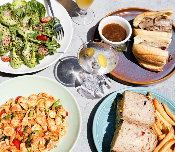 Colorful meal spread includes salad, pasta, sandwiches, fries, and cocktails on a light blue table.